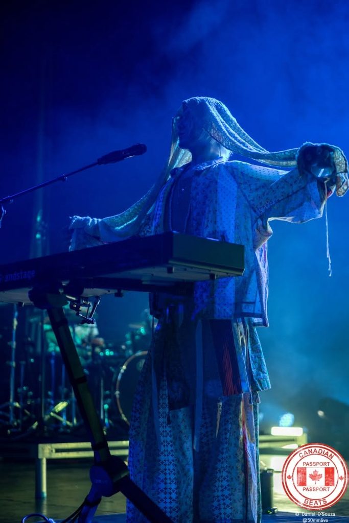 Fujii Kaze spreading his arms and flowing fabric behind a keyboard under dramatic blue stage lighting at HISTORY in Toronto.